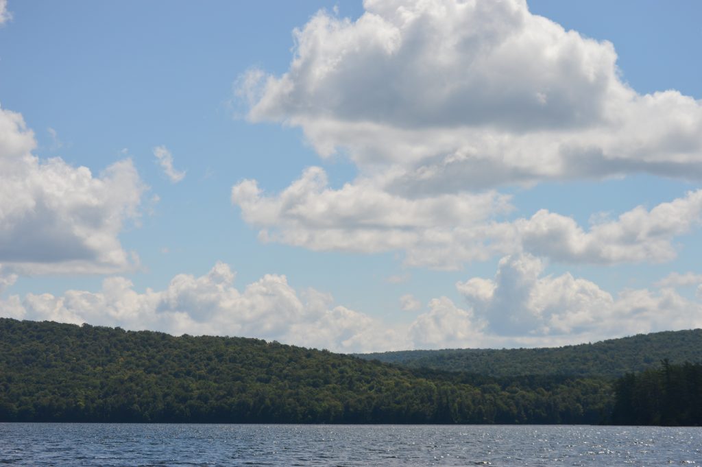 lake in front of hills with fluffy white clouds in the bkue sky